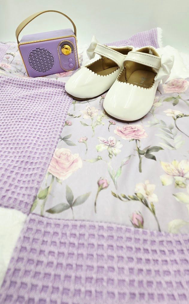 Lavender patchwork baby quilt with floral fabric, white patent leather baby shoes, and a purple vintage-style mini radio.