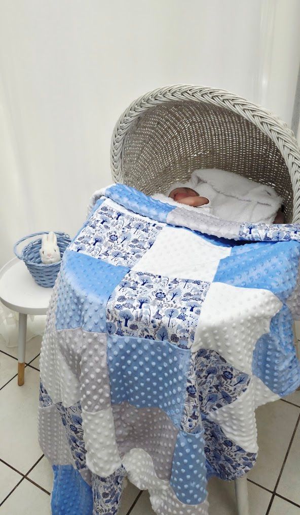 Baby sleeping in white wicker bassinet covered with blue and white patchwork quilt with minky dot fabric squares.