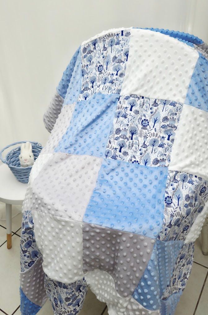 Blue, white, and gray patchwork baby quilt with minky fabric squares, featuring floral print patches draped over a chair.