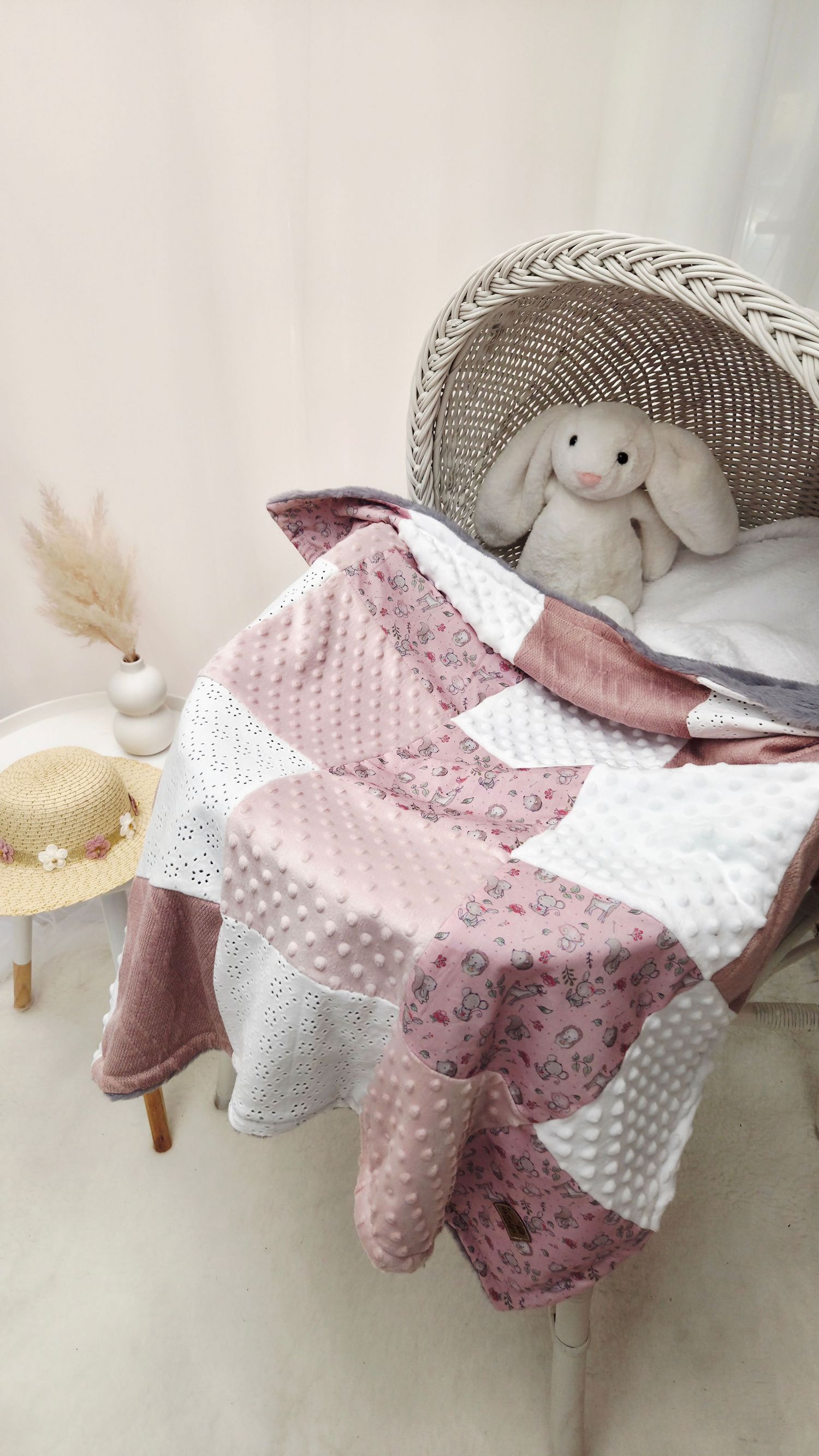 Pink patchwork baby quilt draped over wicker chair with stuffed bunny, featuring minky and floral fabrics.
