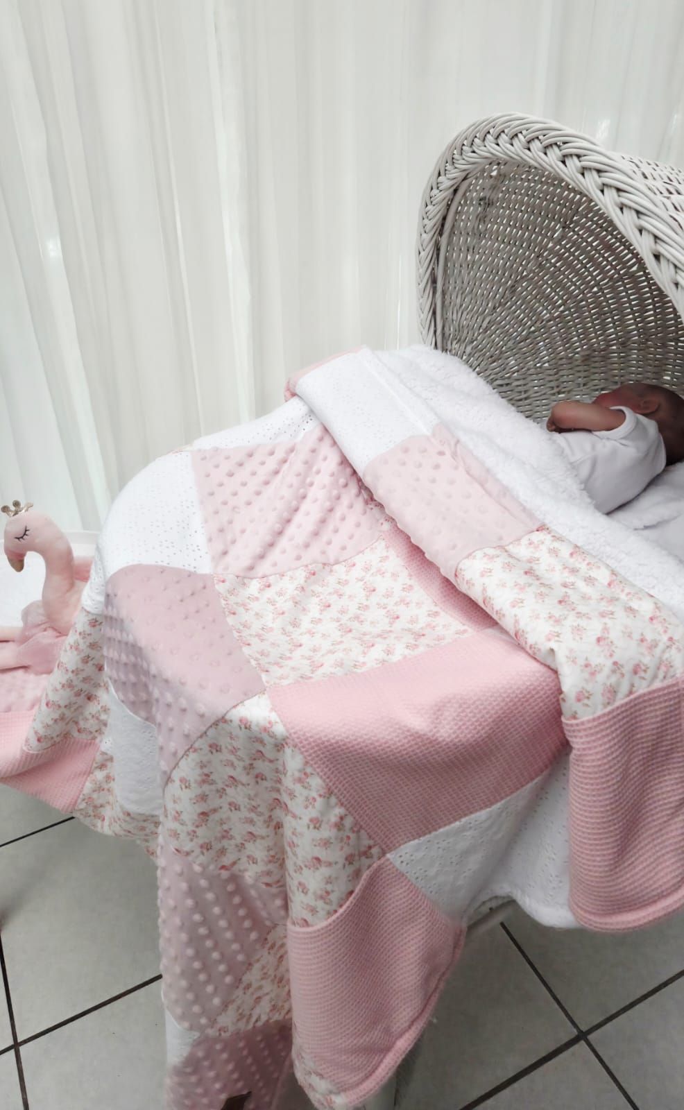 Newborn baby sleeping in a wicker bassinet covered with a pink and white patchwork quilt blanket.