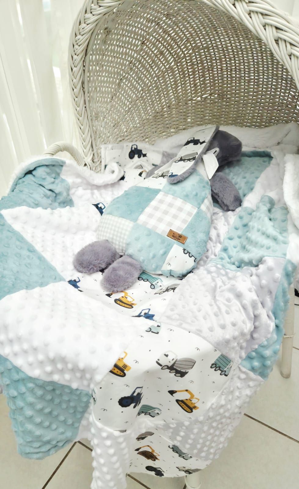Teal and white minky baby quilt set with construction vehicles print, displayed in a wicker bassinet.