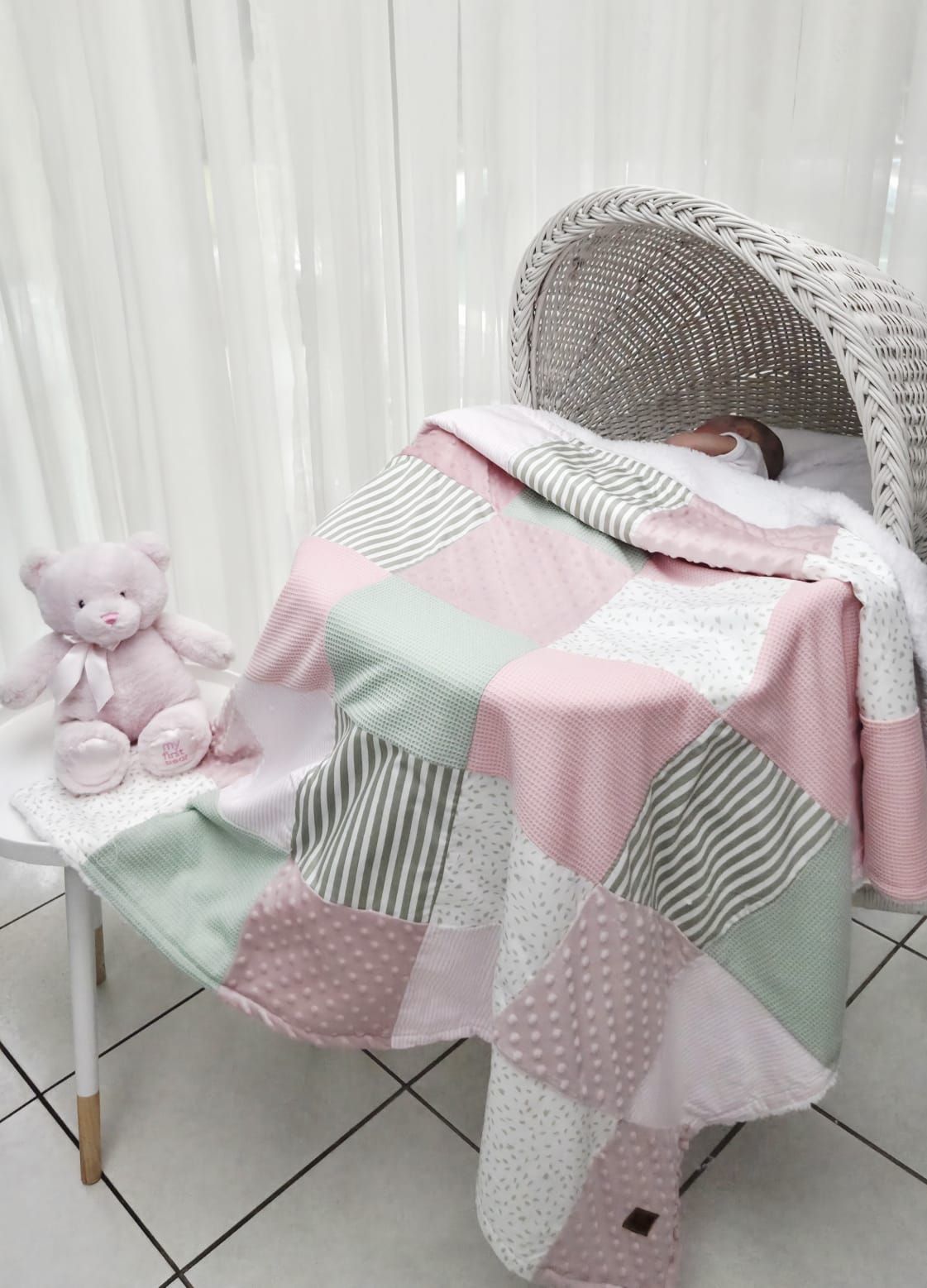 Pink and mint patchwork baby quilt draped over a wicker Moses basket with a pink teddy bear nearby.