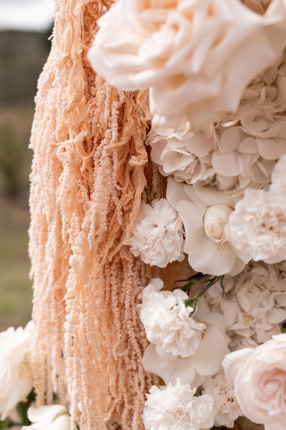 Elegant wedding arch detail with white roses, hydrangeas, and blush peach fringe fabric decoration.