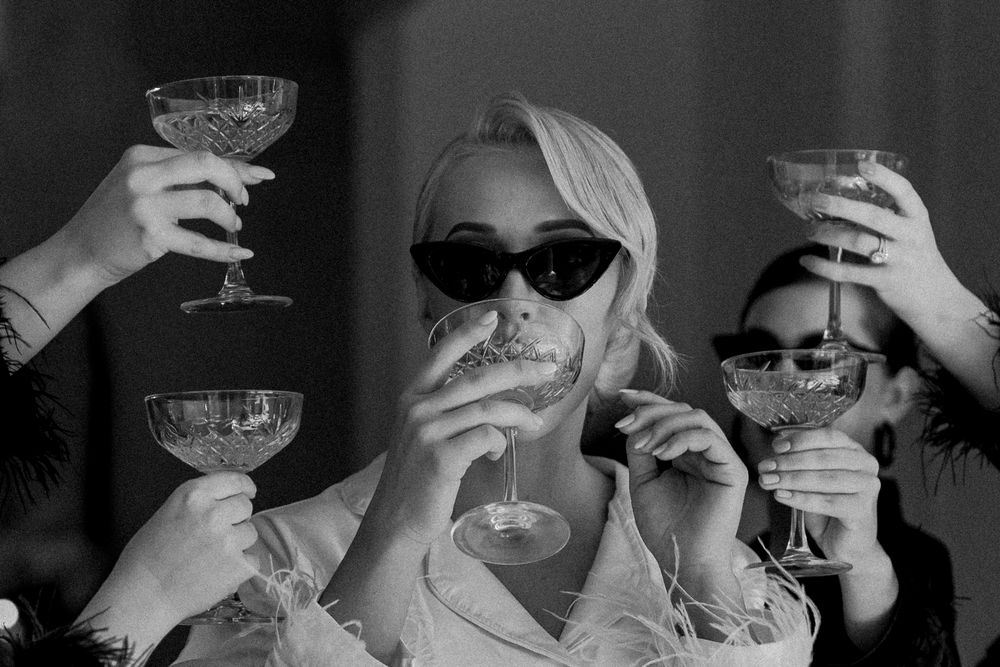 Black and white photo of women in sunglasses toasting with crystal coupe glasses at a celebration.