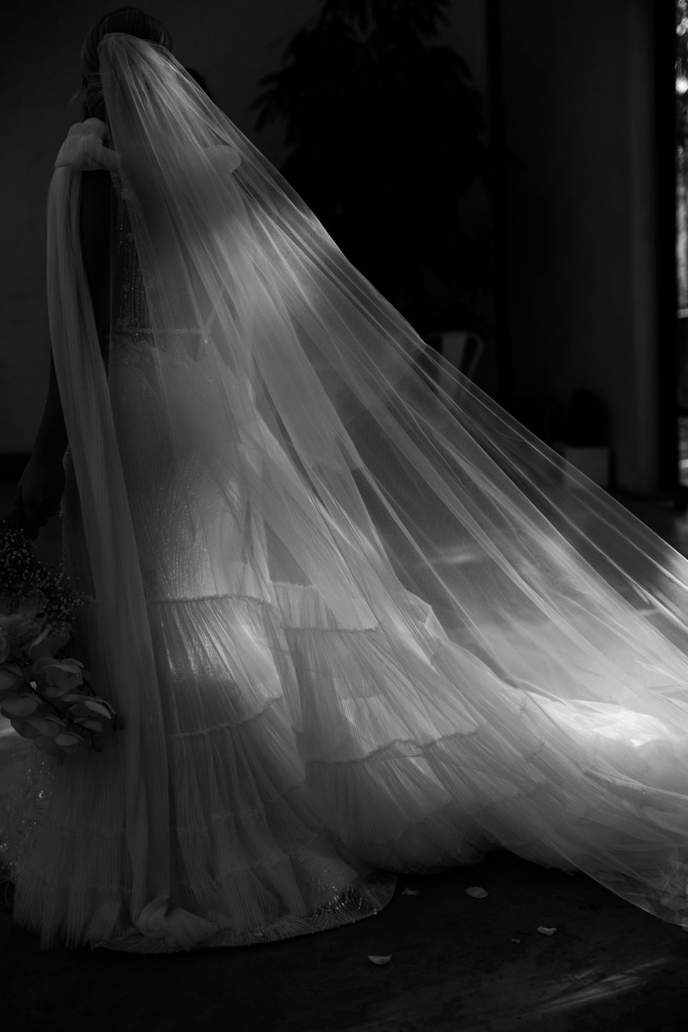 Black and white photo of a bride in a flowing wedding gown with a dramatic billowing veil caught in light.