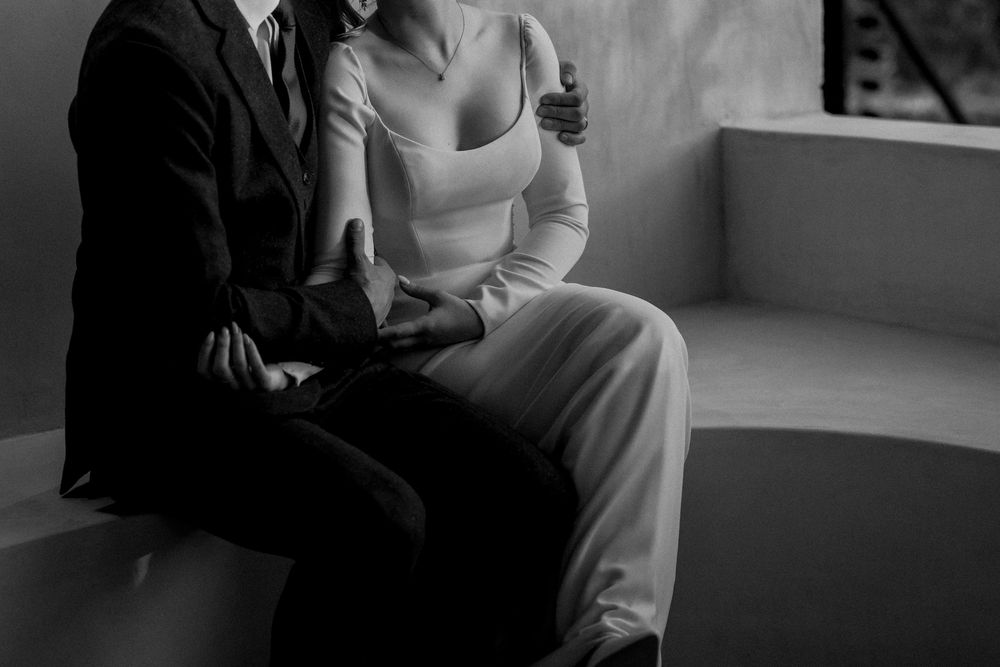 Black and white photo of a couple sitting closely together, holding hands, dressed in elegant formal attire.
