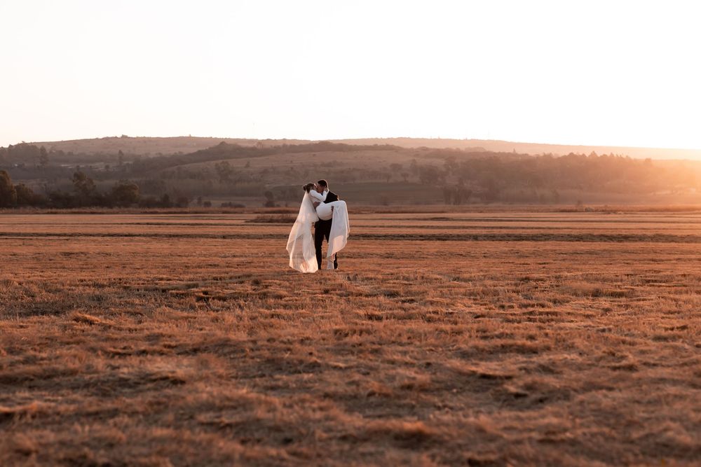 Couple sharing a romantic kiss in a golden field at sunset during their outdoor wedding photoshoot.