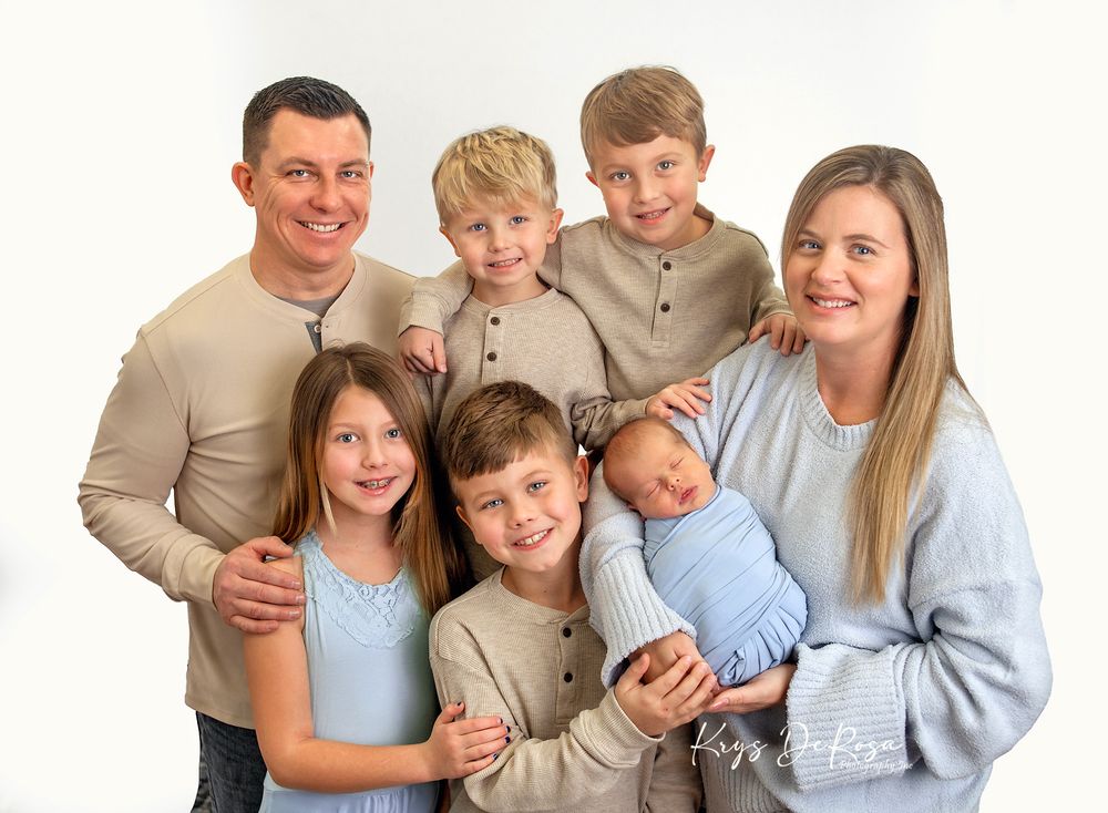 A family group wearing coordinated beige and blue outfits poses together for a professional portrait session.