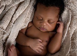 Peaceful newborn baby sleeping wrapped in a soft beige knit blanket in a cozy basket pose.