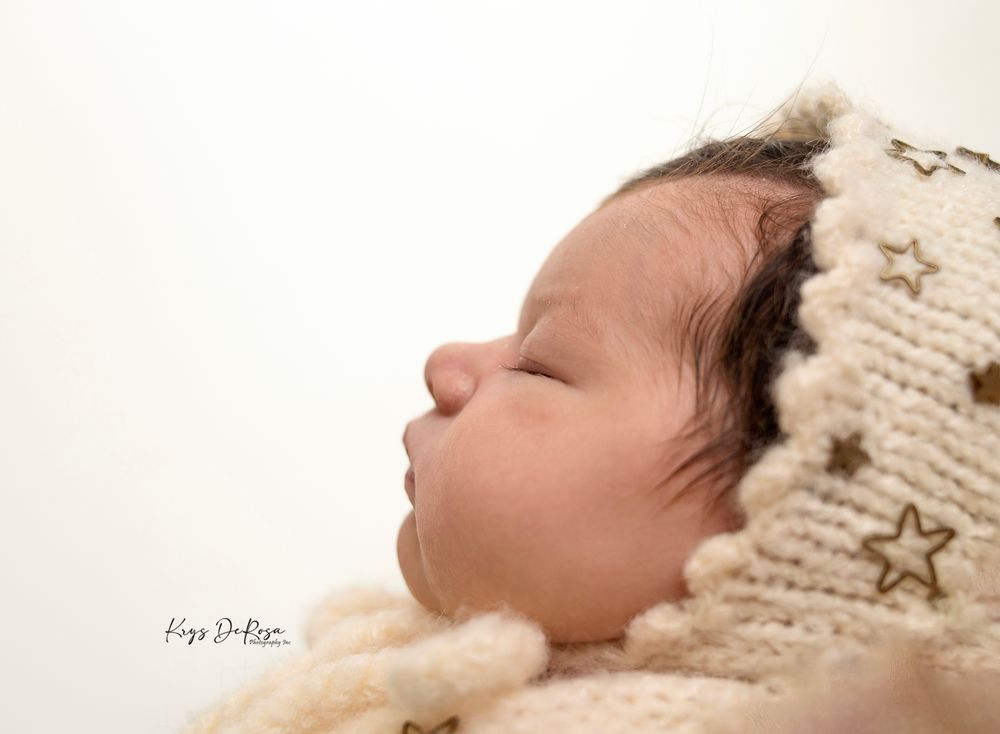 Peaceful sleeping newborn baby wearing a cream knit star bonnet hat in a professional newborn photography portrait.