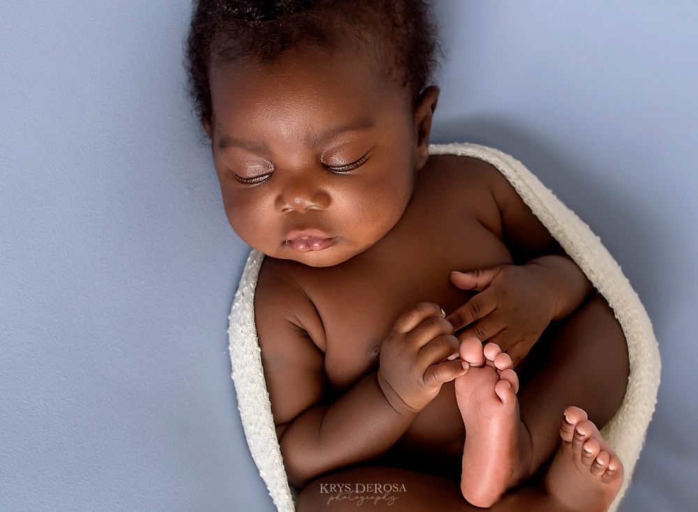 Peaceful sleeping newborn baby wrapped in a soft white blanket on a light blue background in a professional photo.