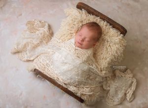 Newborn baby sleeping peacefully in lace wrap on fluffy cream fur in a tiny wooden bed for a professional photo session.
