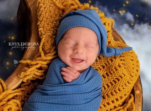 Smiling newborn baby swaddled in blue wrap with mustard yellow knit blanket in wooden bowl by Krys DeRosa Photography.