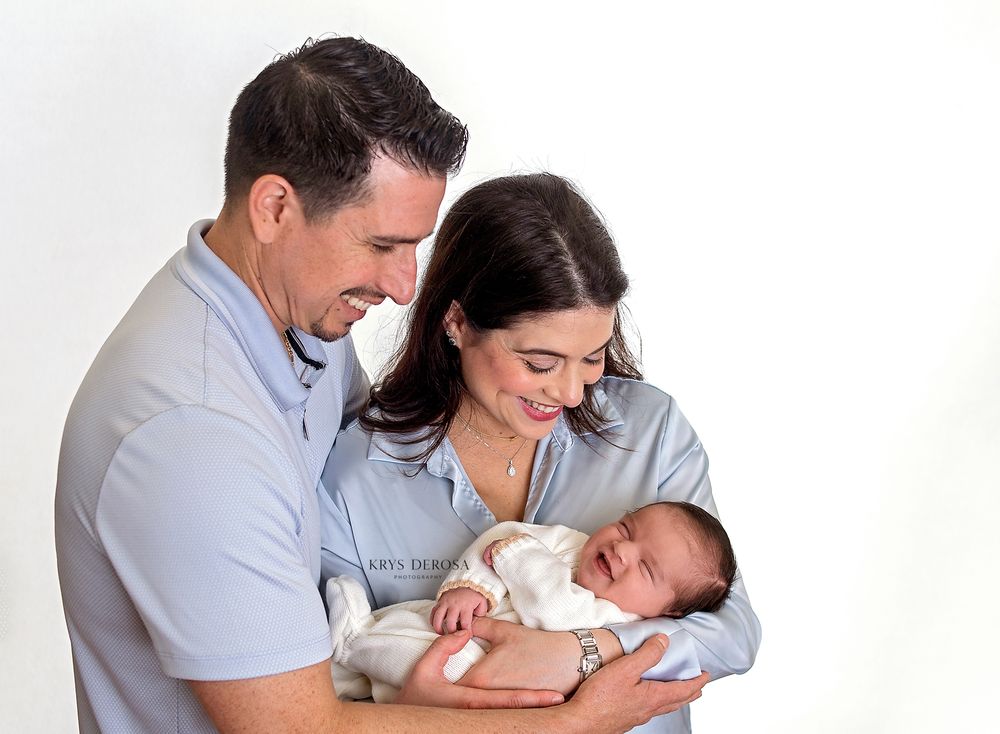 Happy couple smiling at their newborn baby in a bright white studio portrait photo.