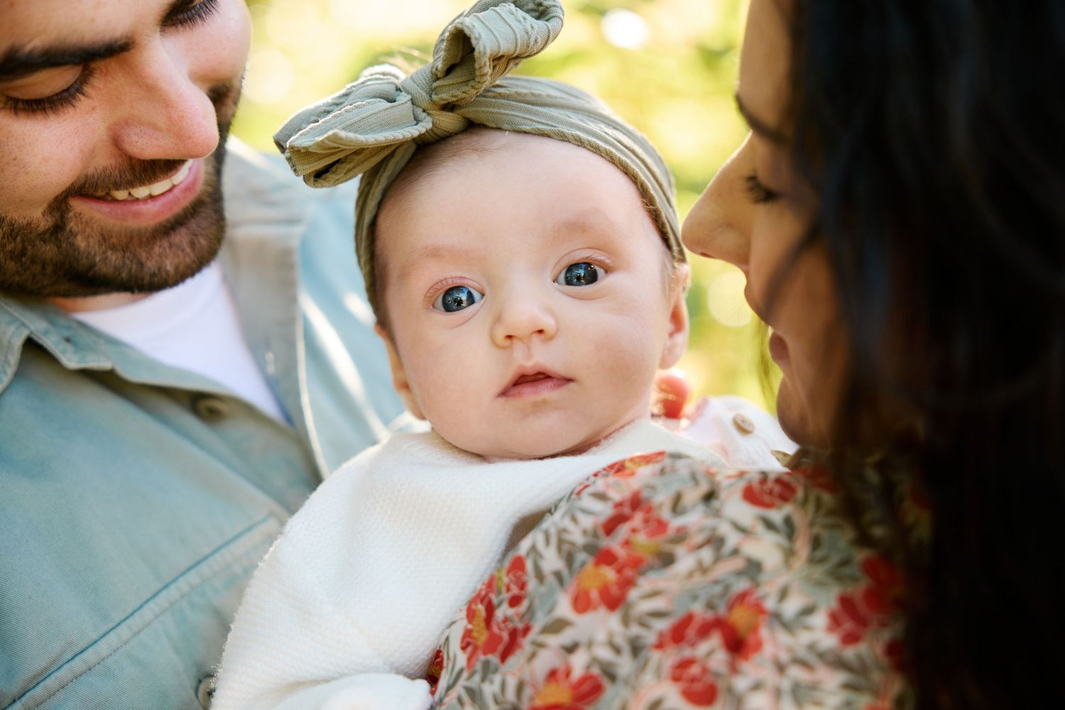 A couple in white and navy blue sits together on a couch while looking at a small baby.