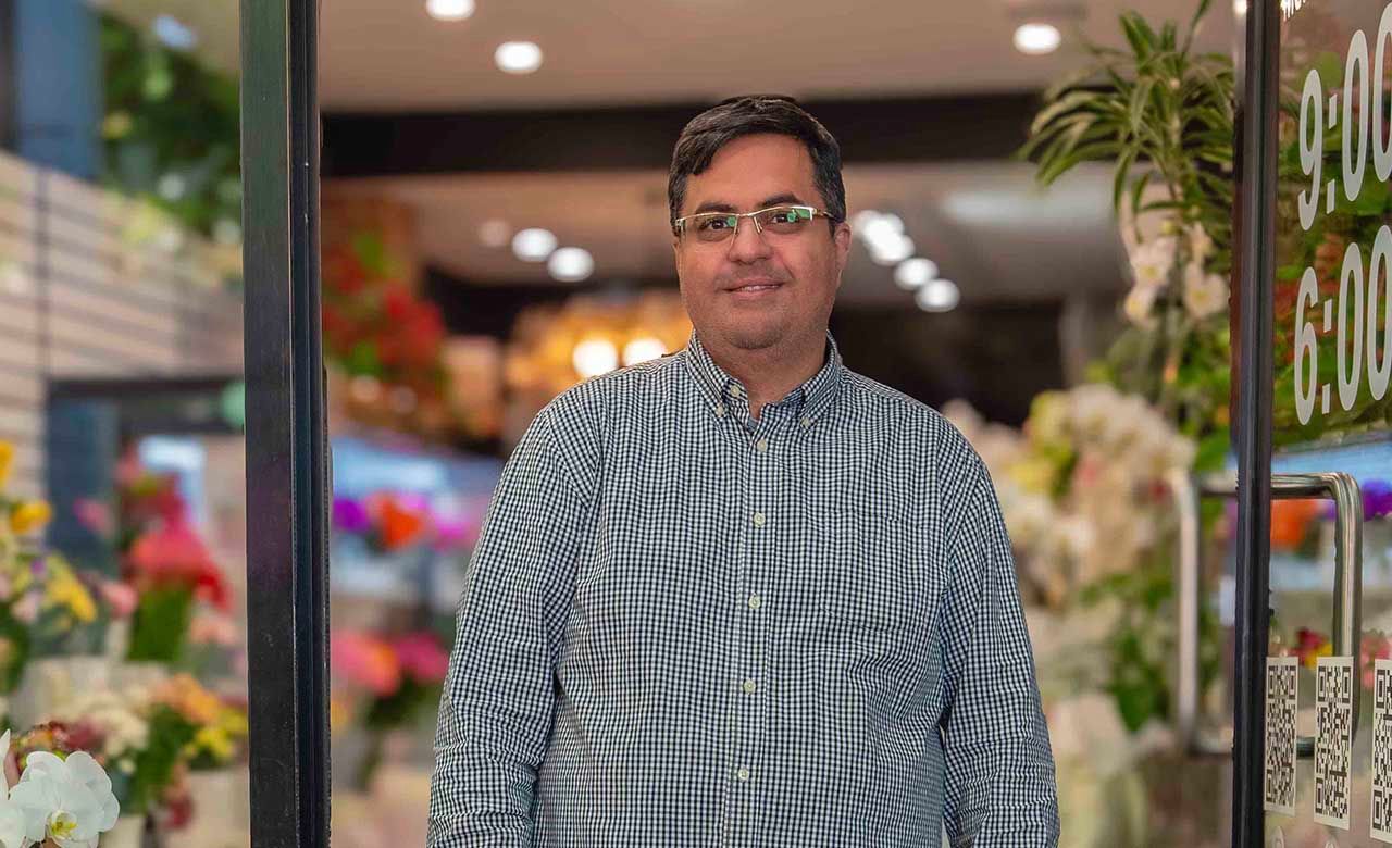 Man in striped shirt standing in front of colorful flower shop display.
