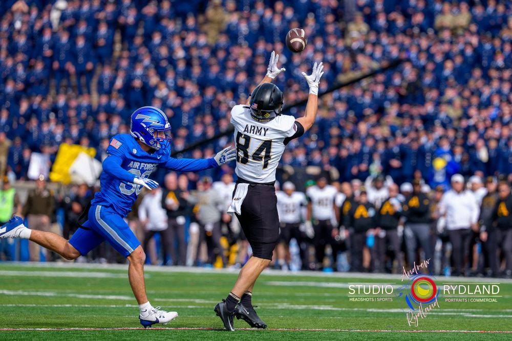 Football player in blue jersey dives to make a catch during an intense game while defender leaps to block.