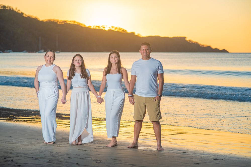 A group stands together holding hands on a golden beach at sunset with mountains in the background.