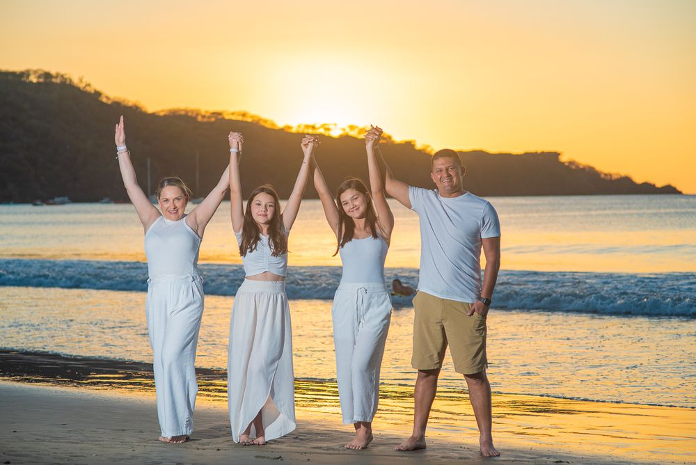 Group of people walking along a beach at sunset with golden light reflecting off the ocean water.