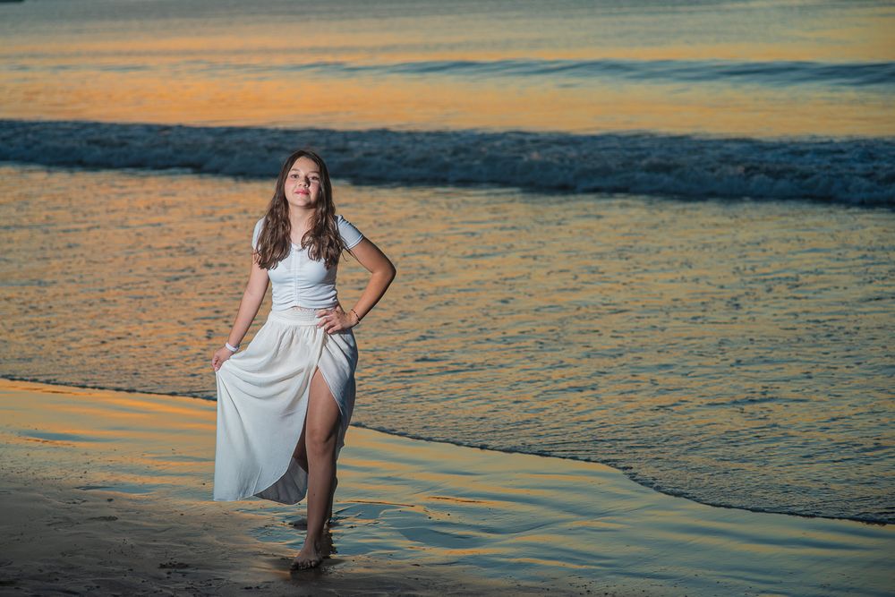 Beautiful sunset beach photoshoot featuring white dress silhouettes against golden ocean waves.