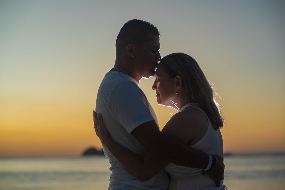 Family photoshoot in Guanacaste; romantic couple embraces while silhouetted against a beautiful sunset on the beach.