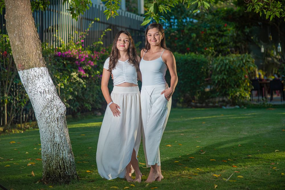 Family photoshoot in Guanacaste, in white dresses hold hands while walking through a lush garden setting on a sunny day.
