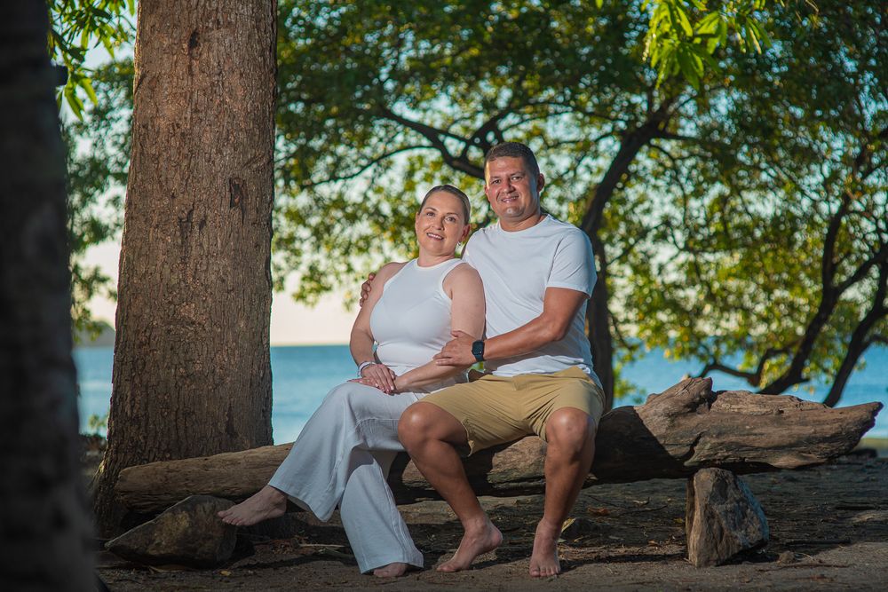 Family photoshoot in Guanacaste, wearing white sits together on a tropical beach at sunset with palm trees in background.