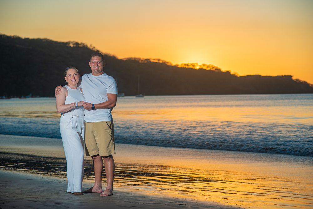 Guanacaste sunset session family enjoying a golden sunset on a beach with calm ocean waters and glowing orange sky in the background.
