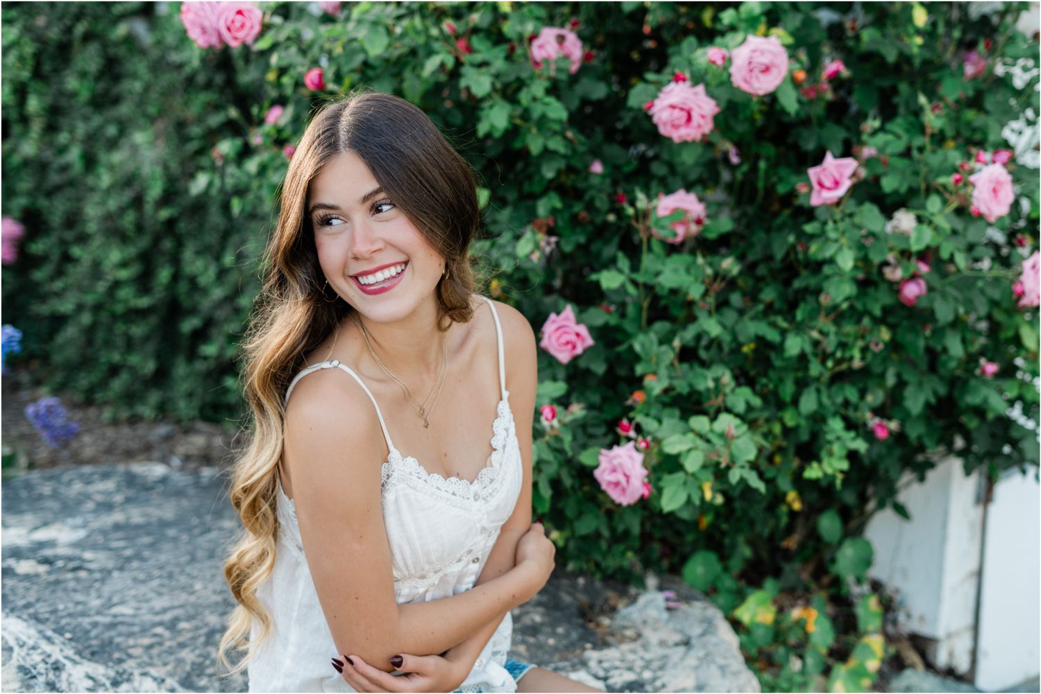 senior wearing white shirt and jean skirt sitting by roses during slo high senior photos by felisha connolly