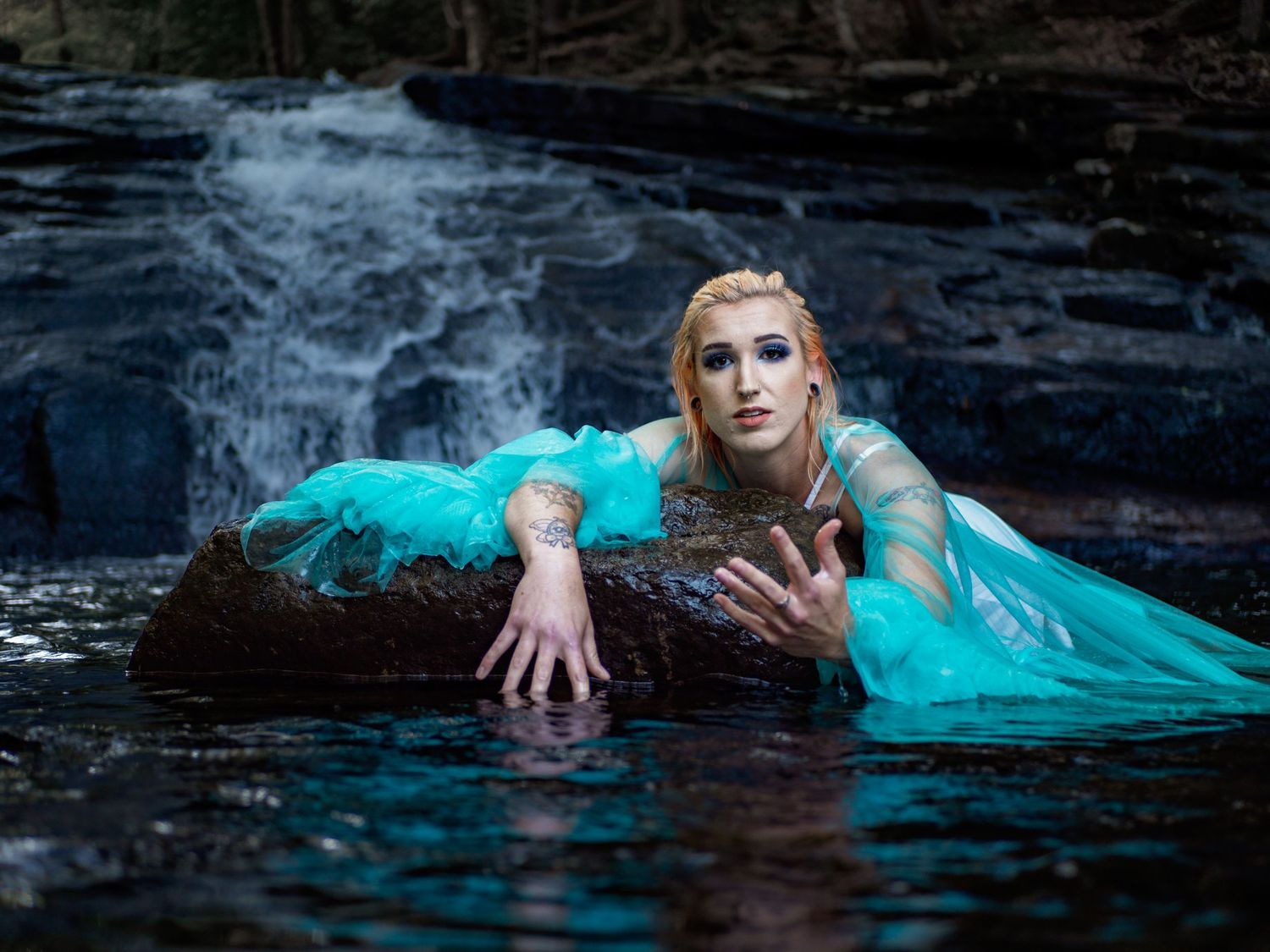 Figure in turquoise dress floats in dark water creating dramatic underwater scene.