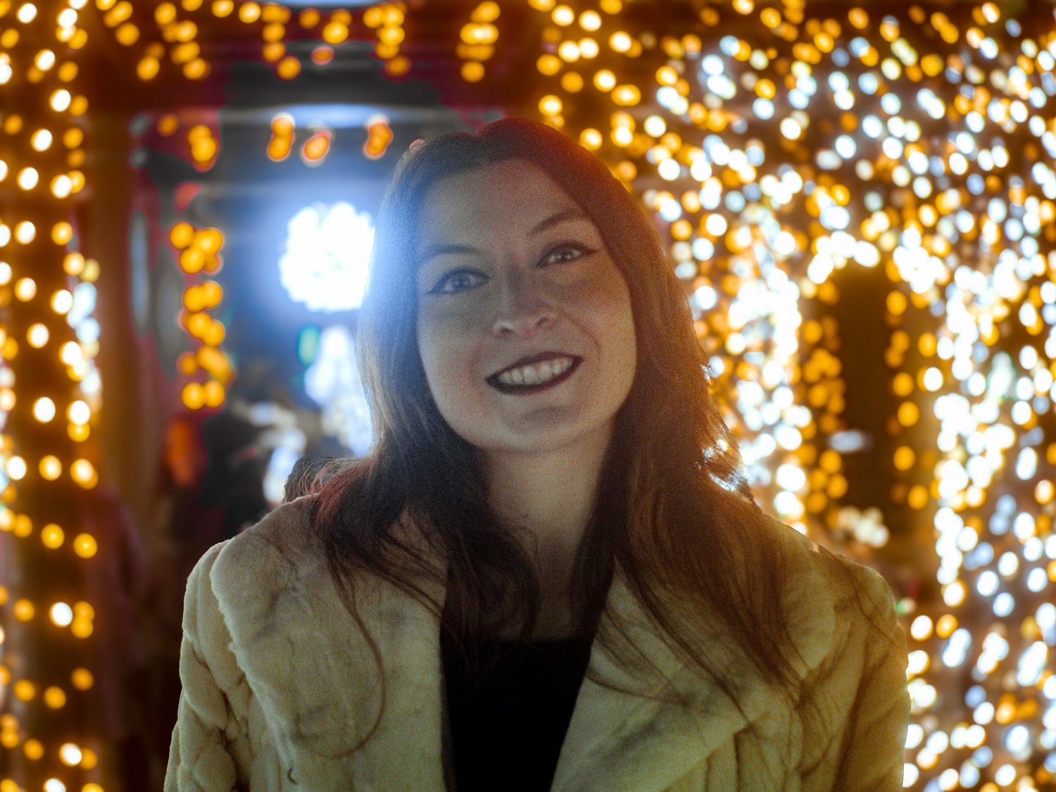 Portrait against warm glowing holiday lights creating festive bokeh effect.