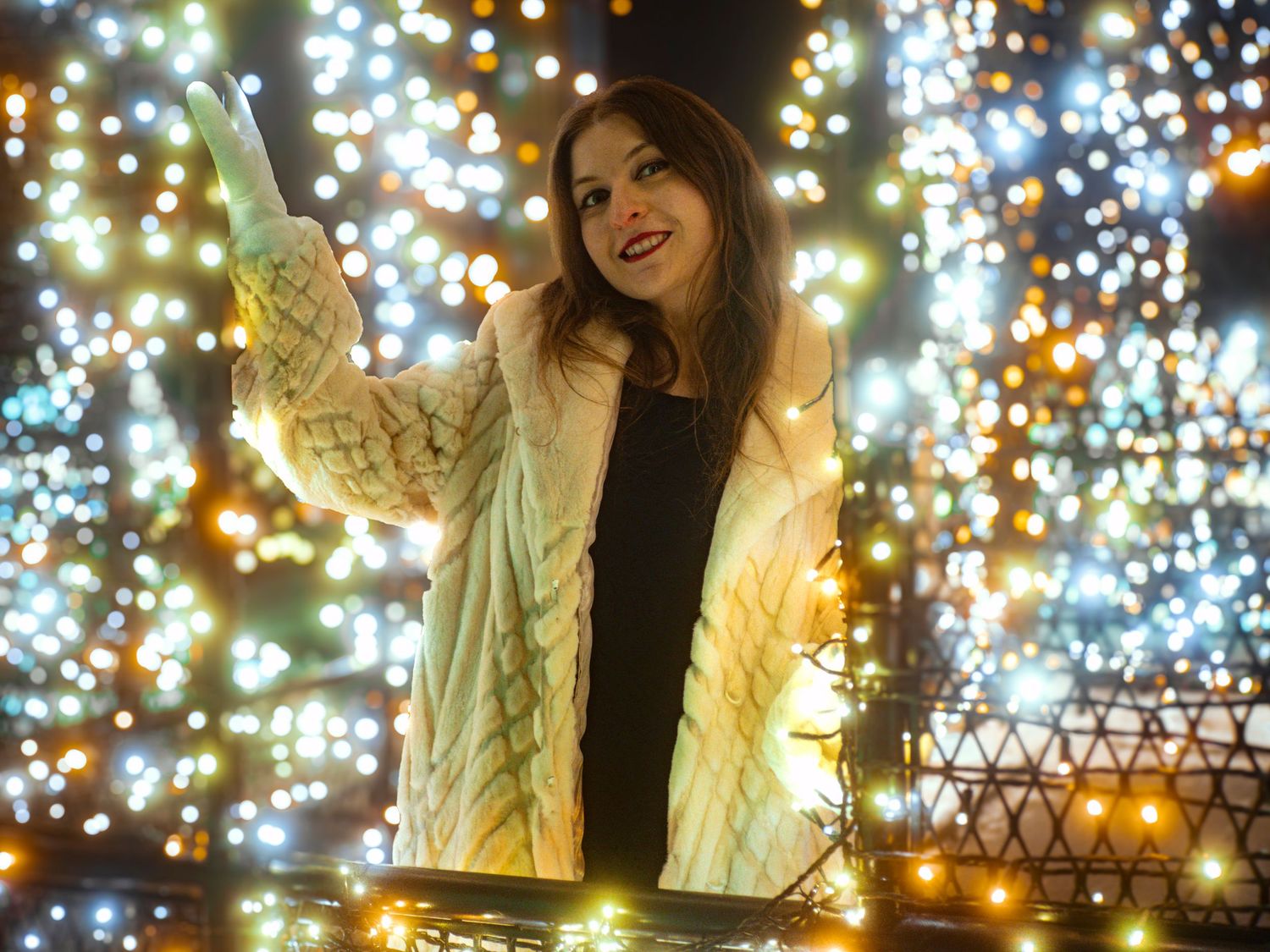 Person in yellow puffer jacket poses against backdrop of twinkling holiday lights creating festive winter ambiance.