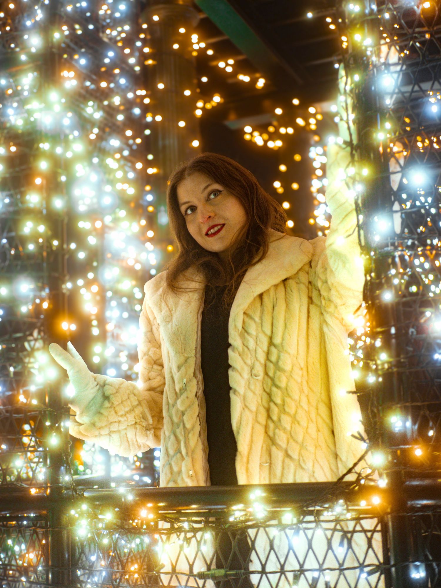 A person poses against a backdrop of twinkling fairy lights while wearing a cream-colored quilted jacket.