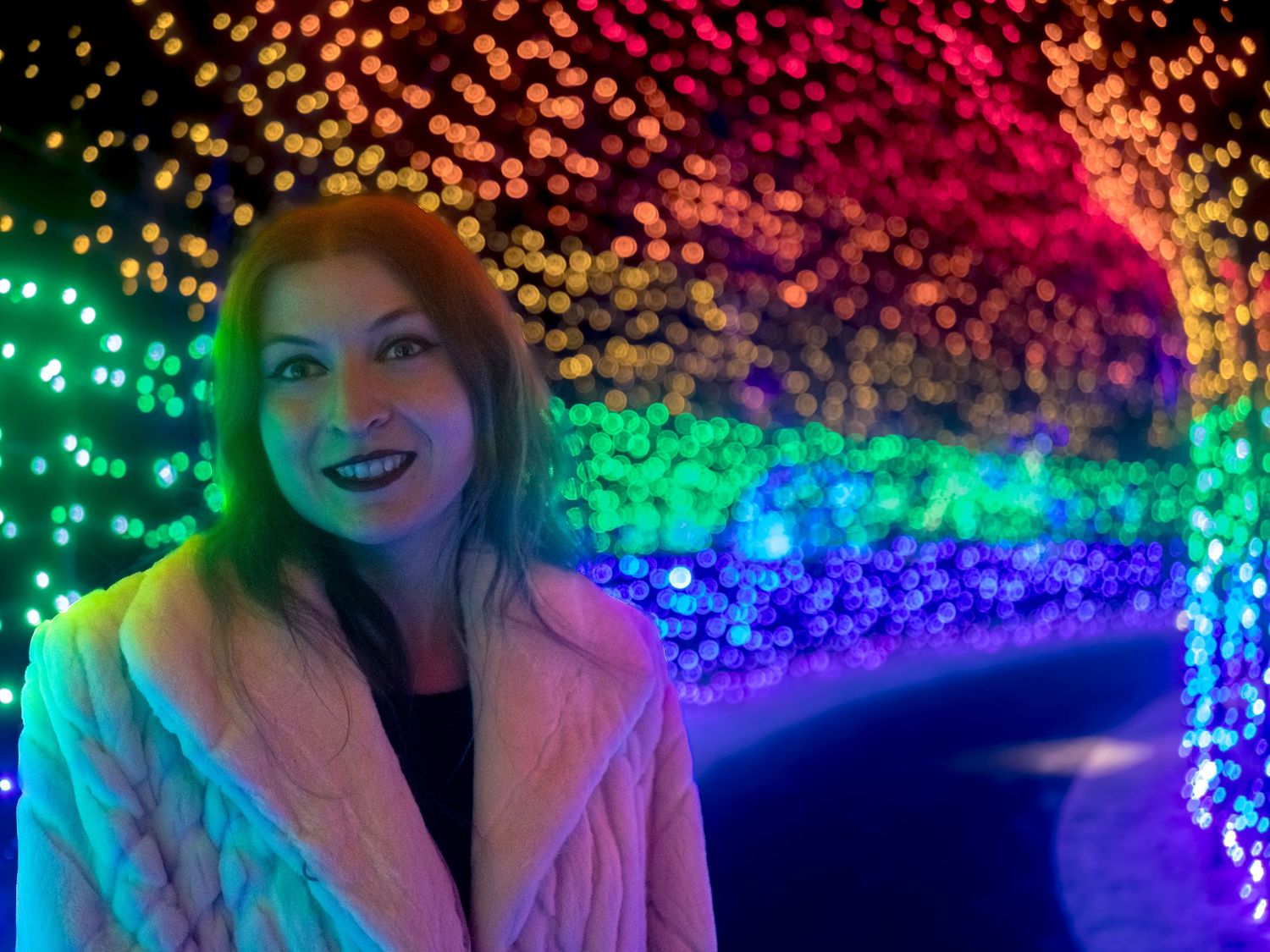Colorful rainbow fairy lights create magical bokeh effect overhead.