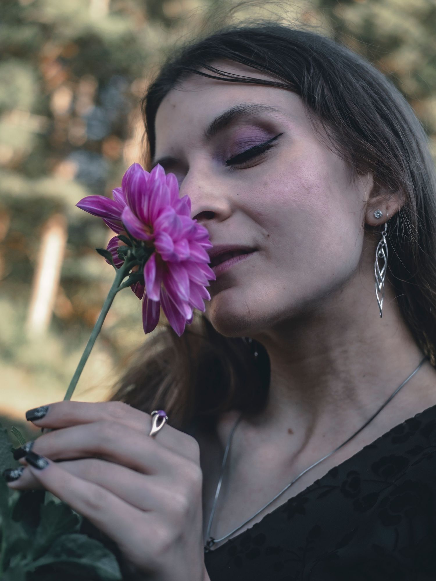 Artistic series showing someone smelling a vibrant purple flower against a moody natural background.