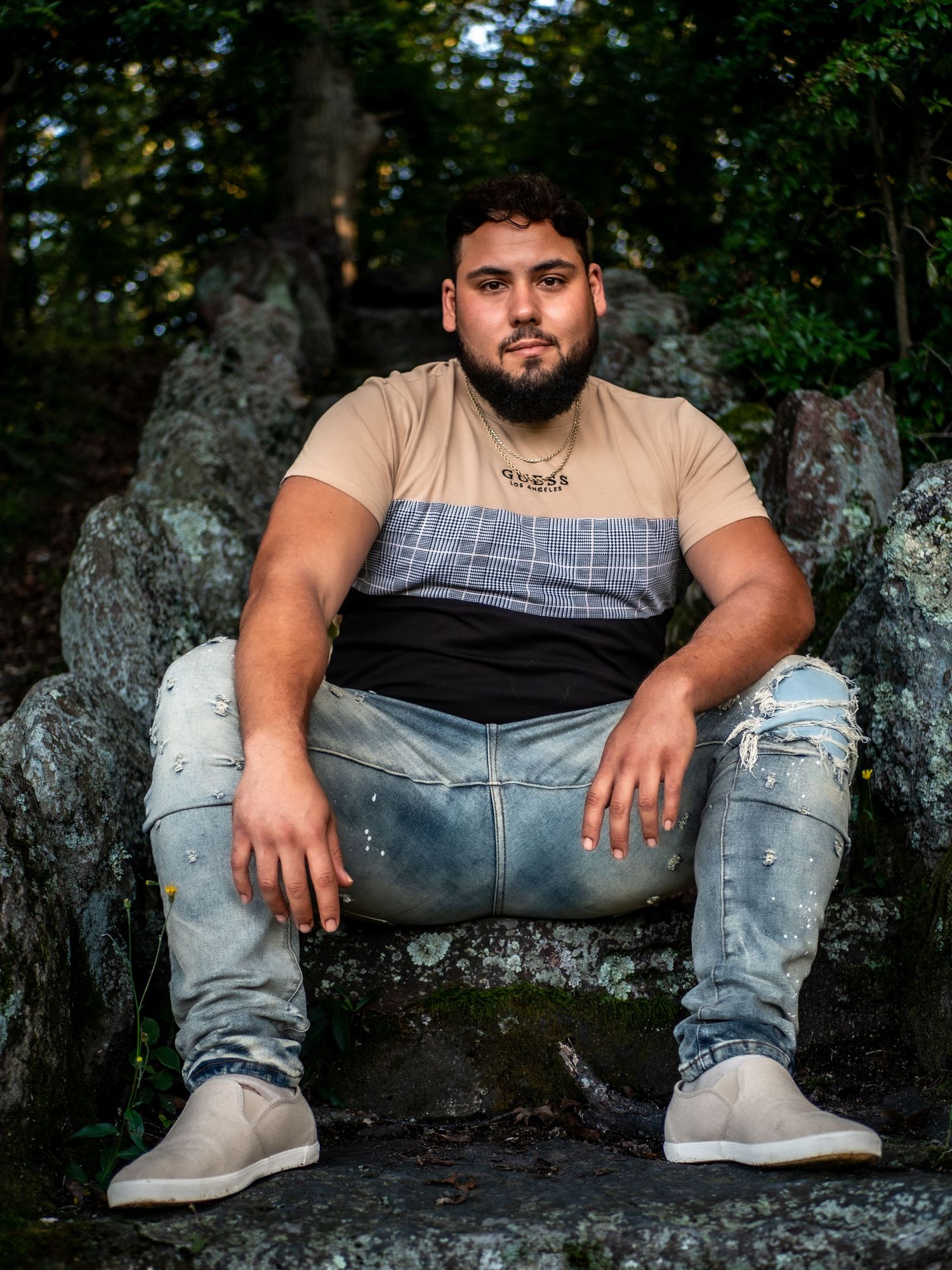 Person wearing casual attire sits on concrete surface against dark foliage background.