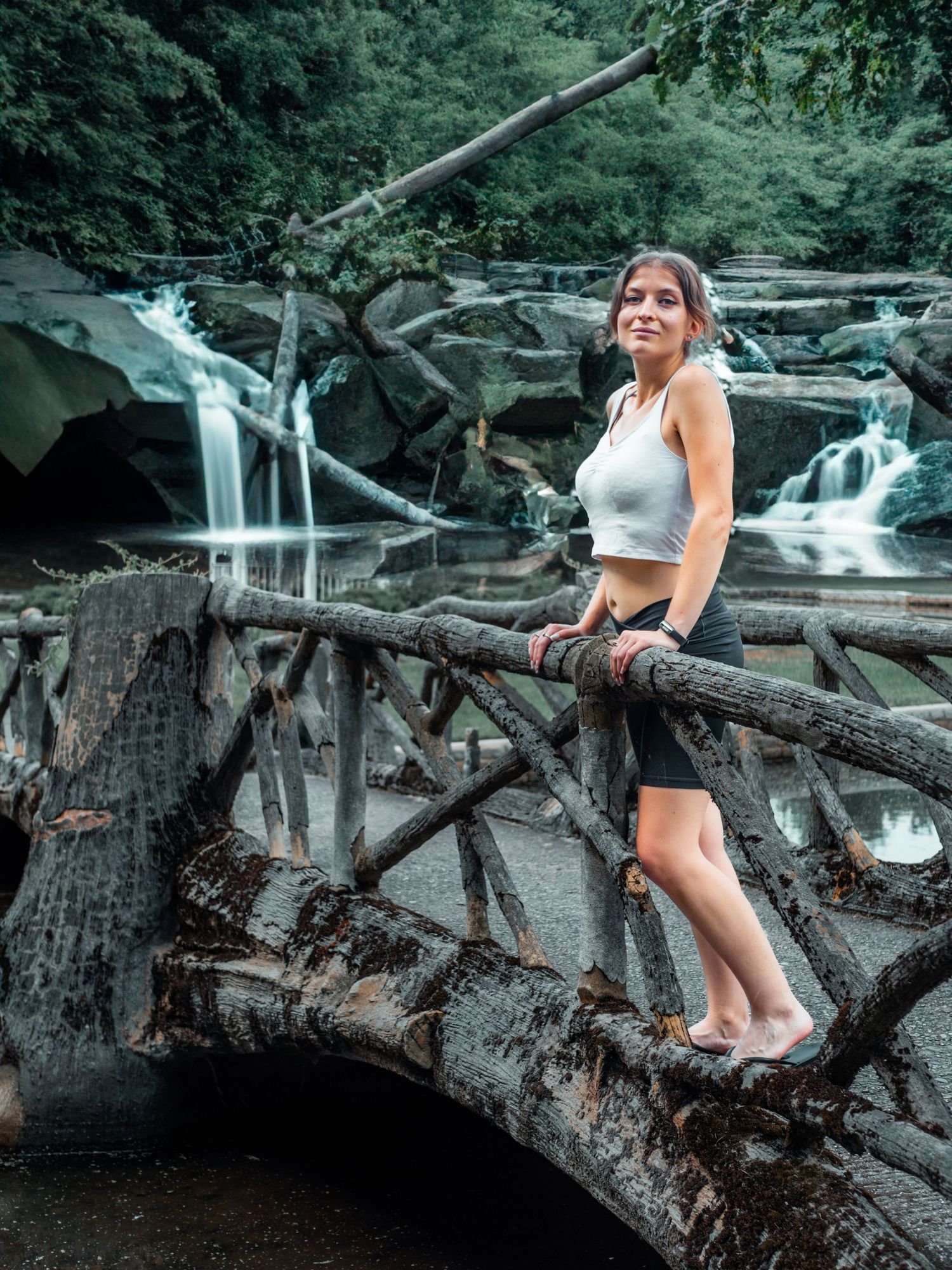 Person sitting on fallen logs near a cascading waterfall in a forest setting.