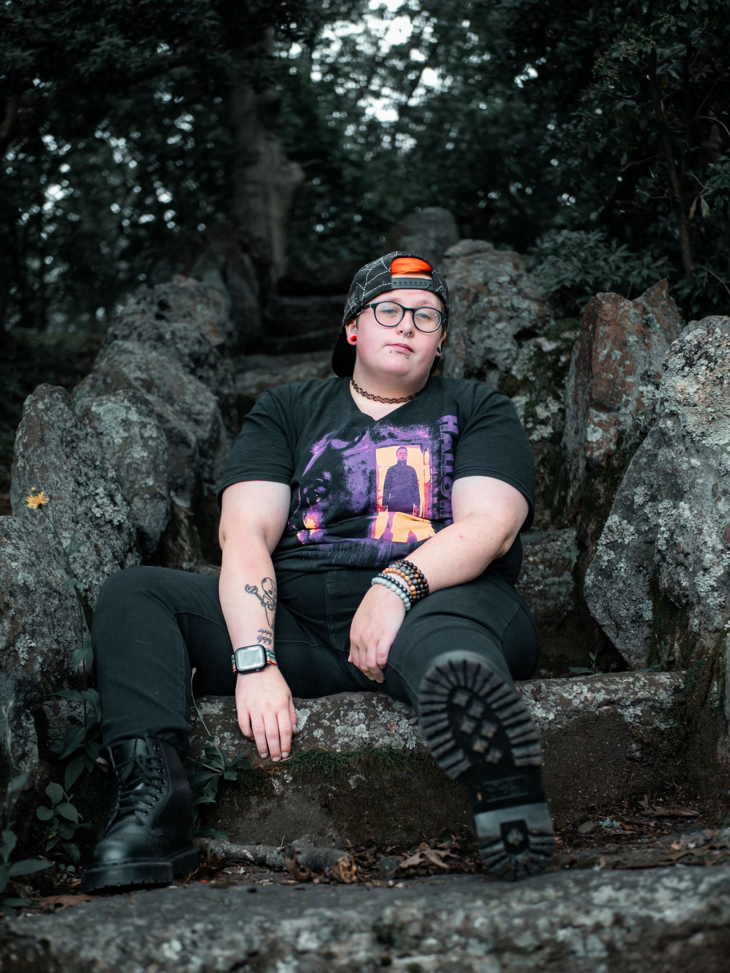 Artistic portrait series showing someone in black boots reclining on dark rocks in a moody forest setting.