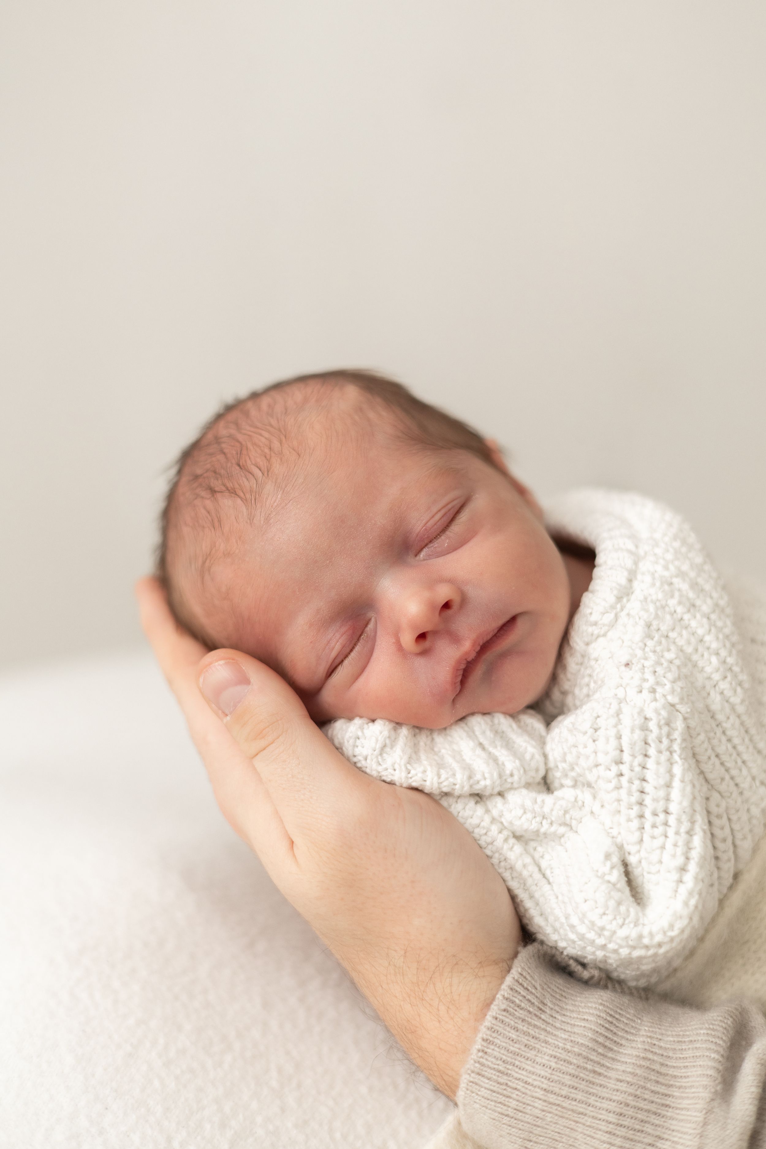 Peaceful newborn baby sleeping in parent's hands, wrapped in a cream knit outfit Nottingham baby photographer studio session