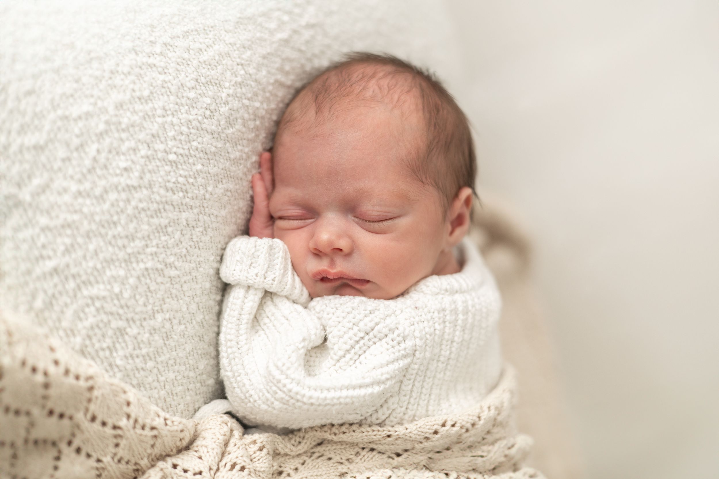 Peaceful newborn baby sleeping wrapped in a soft white knit blanket, perfect newborn photography portrait Nottingham