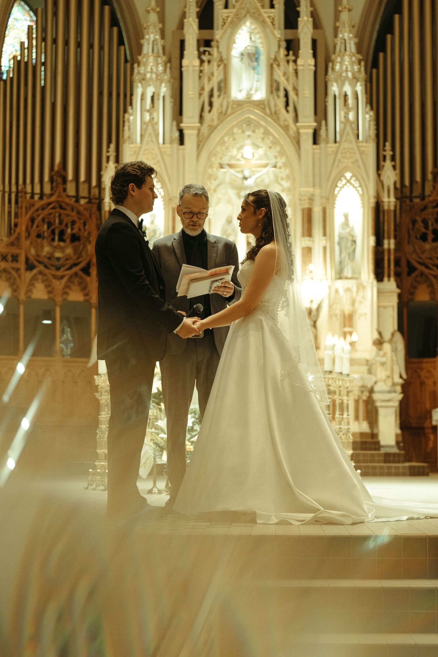 Bride and groom share a first kiss at the altar in a grand cathedral church filled with wedding guests.