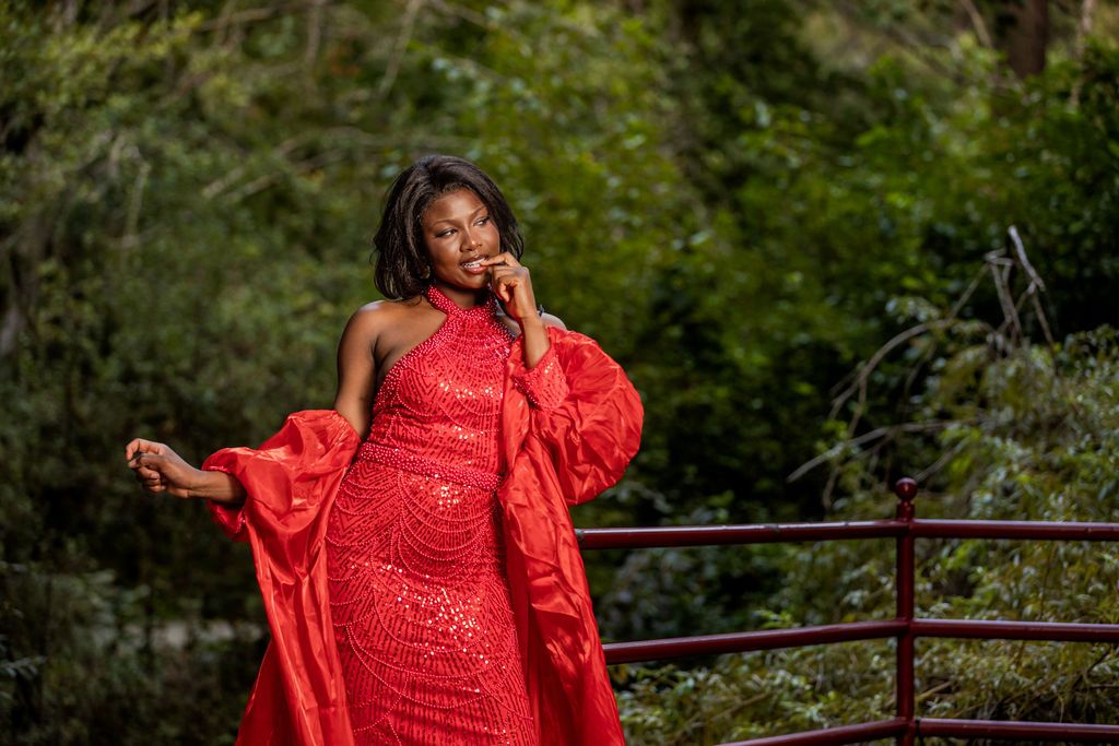 Woman in red sequin dress with puff sleeves posing gracefully on a red bridge.