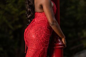 Detail shot of red sequin mermaid dress on woman leaning against red pole.