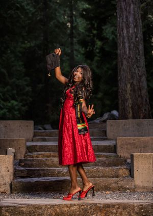 Joyful graduate in red dress holding cap aloft with Class of 2025 stole outdoors.