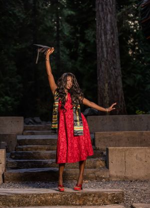 Graduate celebrating in red dress raising cap with Class of 2025 kente stole.