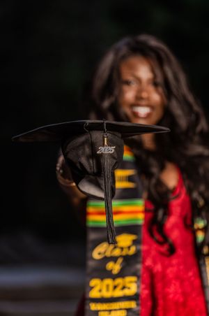 Close-up of Class of 2025 graduation cap held forward with smiling graduate behind.