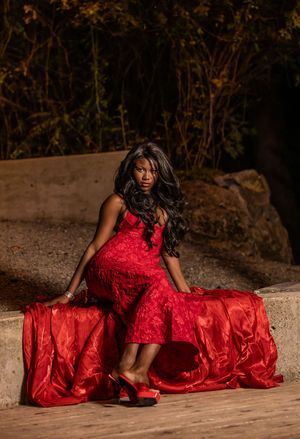 Woman in red flowing gown seated gracefully on stone ledge at night outdoors.