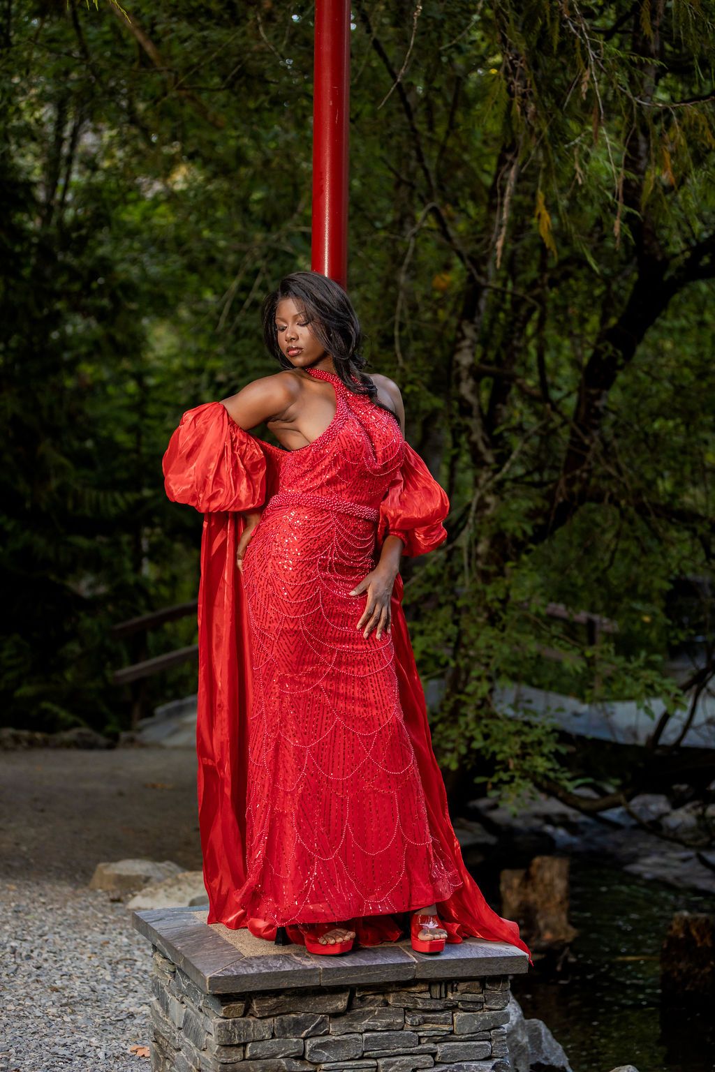 Woman in elegant red sequin dress with puff sleeves standing on stone pedestal.