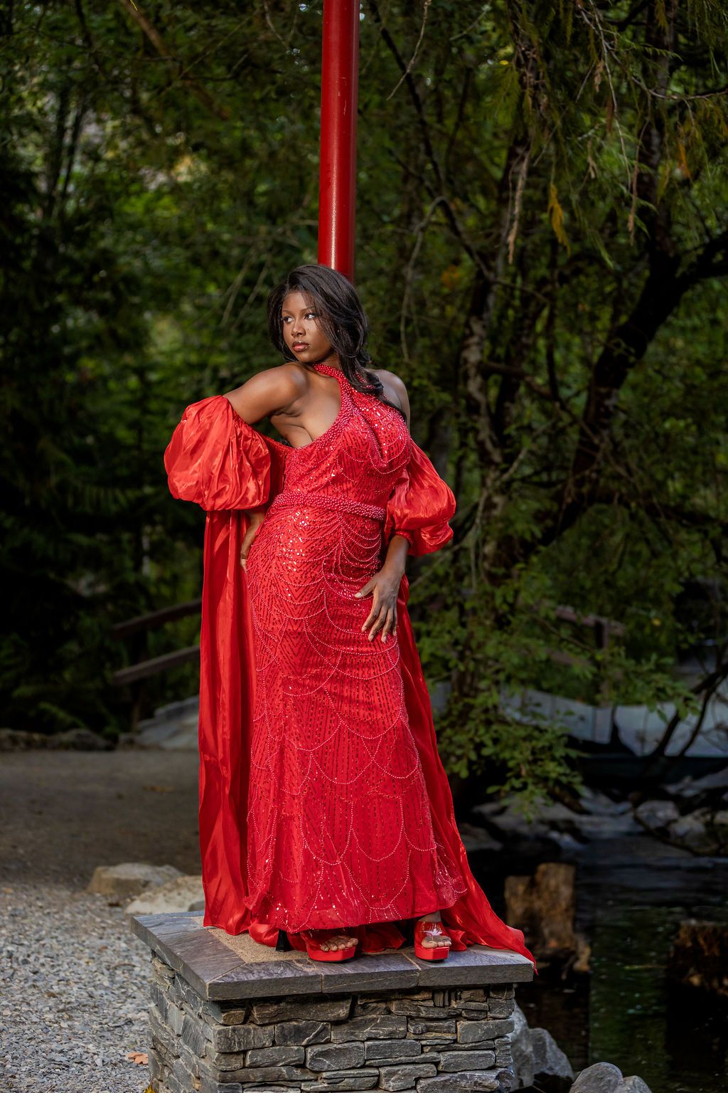 Woman in red sequin dress with billowing sleeves posing on a stone platform outdoors.